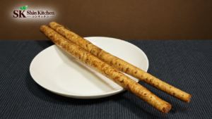 白い皿に置いた2本のごぼうと、左上のShin Kitchen共通ロゴ